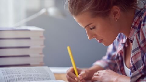 Eine junge Frau lernt und schreibt; neben ihr ein Stapel Bücher