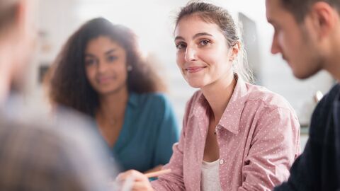Eine Frau sitzt neben weiteren Lernenden und schaut den Betrachter an 