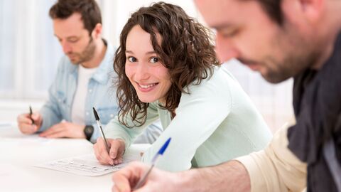 Zwei Männer und eine Frau, die gerade einen Kurs besuchen und ein Arbeitsblatt ausfüllen