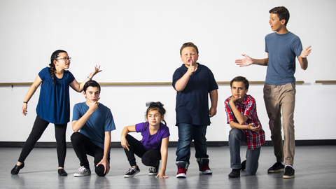 Kinder in Turnkleidung, die Posen und Gesichtsausdrücke mit einem Lehrer üben