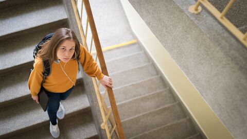 Eine Schülerin steigt die Treppen einer Schule hinab; sie blickt den Betrachter nachdenklich an  