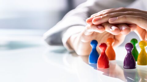 Zwei Hände werden schützend über bunte Spielfiguren gehalten