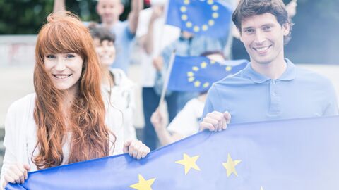 Erasmus+ Jugendliche, die EU-Fahnen hochhalten und den Betrachter anblicken
