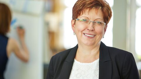 Eine Frau im besten Alter im Büro; im Hintergrund ein Flipchart