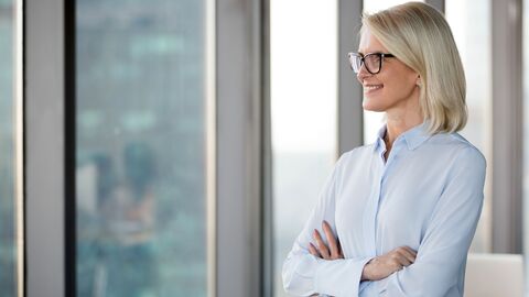 Frauenbeauftragte und Gleichstellung  Eine Frauenbeauftragte, die mit vor dem Körper verschränkten Armen aus dem Fenster ihres Büros schaut