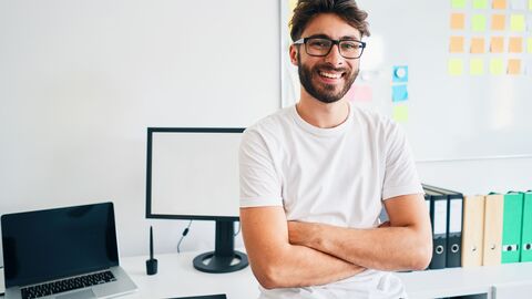 Ausbildungsplatz Ein leger gekleideter junger Mann im Büro; er verschränkt die Arme und lächelt den Betrachter an