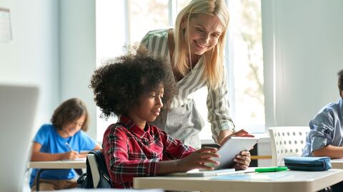 Hospitationen im Ausland  Lehrerin in einem Klassenraum an einem Schülertisch; sie spricht mit einer Schülerin