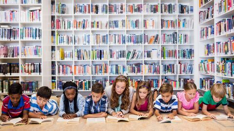Leseförderung Schüler, die nebeneinander auf dem Boden liegen und in einer Bibliothek lesen