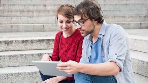 Eine Lehrerin und ein Lehrer, die auf einer Treppe sitzen und auf ein iPad schauen