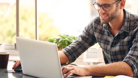 Ein Mann in kariertem Hemd, der vor seinem Notebook sitzt
