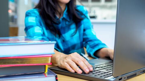 Kontaktformular  Eine Frau tippt auf ihrem Laptop; neben ihr ein Stapel Bücher