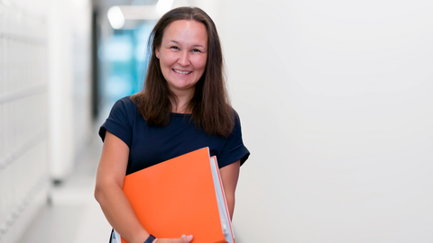 Eine Lehrerin mit einer orangen Mappe im Flur