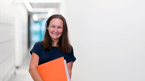 Eine Lehrerin mit einer orangen Mappe im Flur