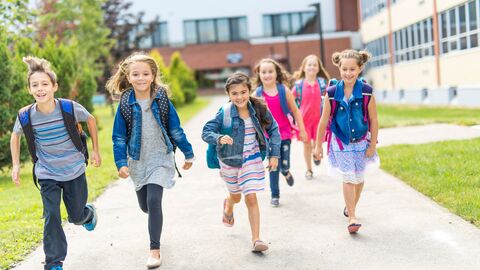 Kinder mit Schultaschen rennen an dem Gebäude einer Schule entlang