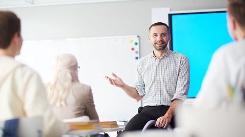 Lehrer sitzt im Unterricht auf dem Pult und erklärt 